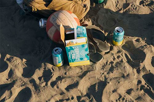 a beer box open with a cans an volleyball ball in a sand