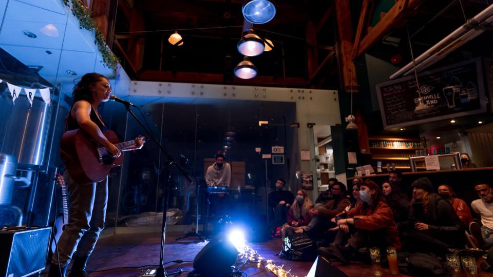 Girl song and play the guitar on bar with people listening